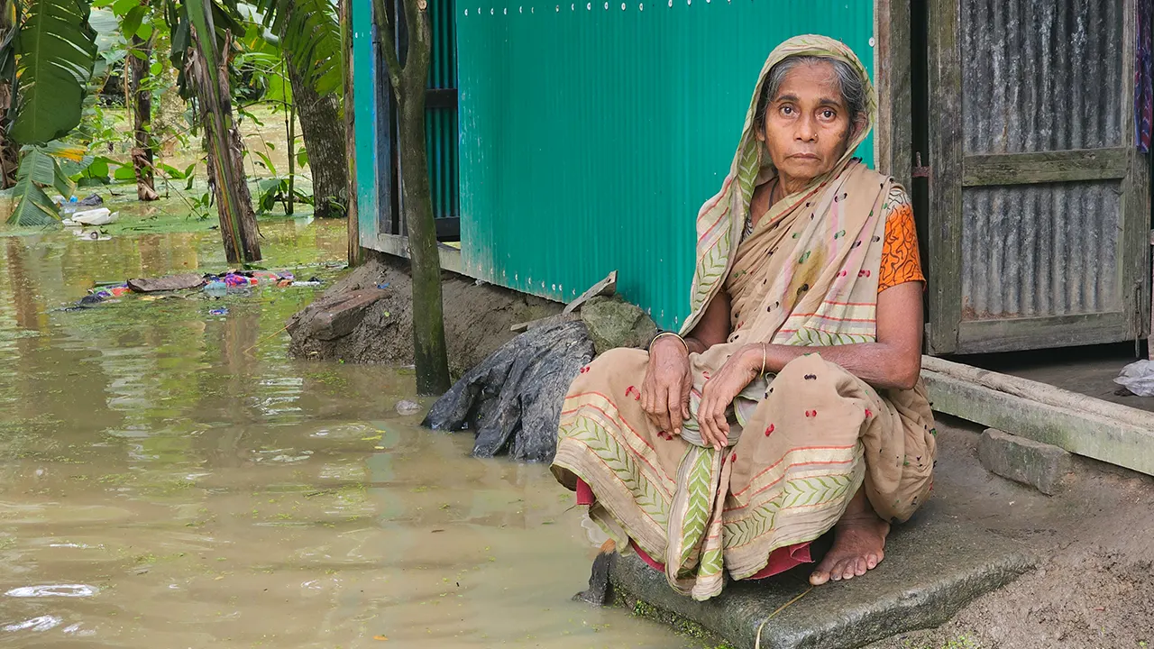 ঘরের দরজায় বসে ত্রাণের জন্য অপেক্ষা করছেন আনোয়ারা বেগম। ছবি : কালবেলা